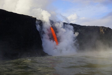 Fototapeta na wymiar Stream of hot lava flowing down from high Cliff surrounded by white steam, Hawaii Big Island