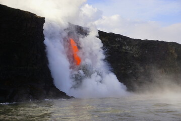Lava flows down from high cliff into the ocean  surrounded by white steam, Big Island in Hawaii