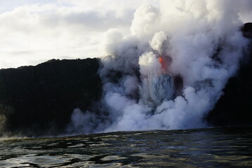 Hot lava stream flowing down from high cliff  into the ocean surrouded by white steam