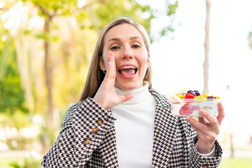 Young blonde woman holding a three dimensional puzzle cube at outdoors shouting with mouth wide open
