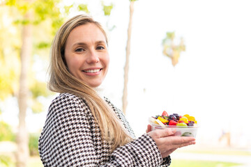 Young blonde woman holding a three dimensional puzzle cube at outdoors smiling a lot