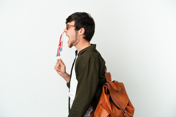 Young Russian man holding an United Kingdom flag isolated on white background laughing in lateral position