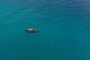 Fototapeta na wymiar Scoglio isolato in mezzo al mare blu con onde concentriche tutt'attorno