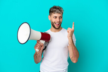 Young handsome caucasian man isolated on blue background holding a megaphone and intending to...