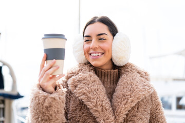Young woman wearing winter muffs  and holding take away coffee at outdoors with happy expression