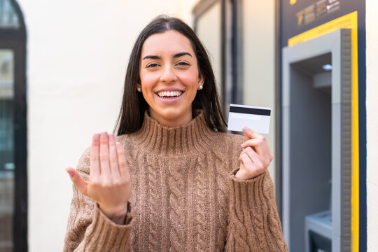Young woman holding a credit card at outdoors inviting to come with hand. Happy that you came