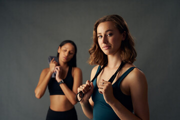 Confident young women in sports clothing holding jump rope over shoulder while looking at camera