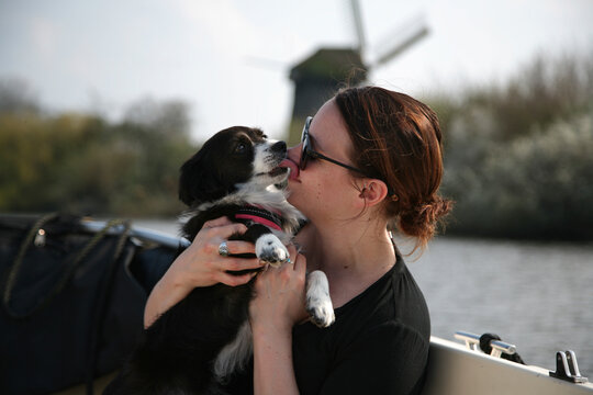 A young woman getting licked by her dog on a boat ride.