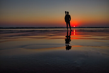 Silhouette of a woman on the beach at sunset, reflection in water.