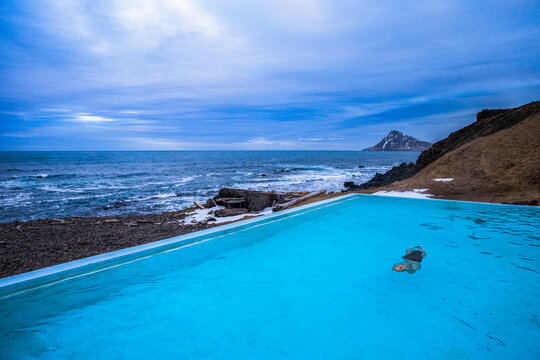 A woman swiming in a geo thermal heated pool on the beach near Nordurfjordur, Iceland