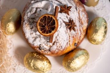 Easter Kulich decorated with cinnamon and dried orange, with golden Easter eggs next to it on a light background