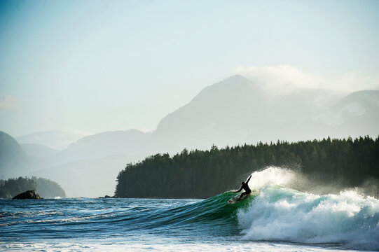 Surfer turns at sunrise on wave with mountains in background
