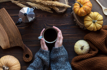 Hands with a cup of coffee with pumpkins on the table