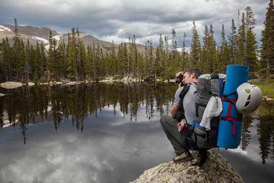 A man takes pictures from a boulder on the shore of Chipmunk Lake, Rocky Mountain National Park, Colorado.