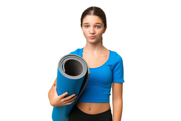 Teenager caucasian girl going to yoga classes while holding a mat over isolated background with sad...