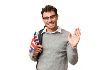 Brazilian man holding an United Kingdom flag over isolated chroma key background saluting with hand with happy expression
