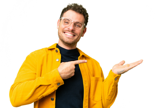 Brazilian man over isolated chroma key background holding copyspace imaginary on the palm to insert an ad