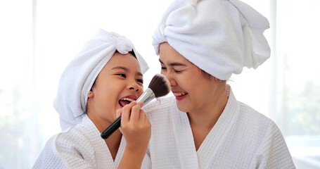 Happy Asian daughter and mother playing makeup after bathroom sitting on bed together at home, Family and beauty concept