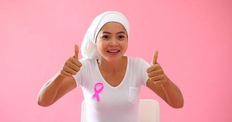 Asian female cancer patient wearing headscarf with pink breast cancer awareness ribbon smiling and supporting talking on at camera cheering give empathy to breast cancer patient