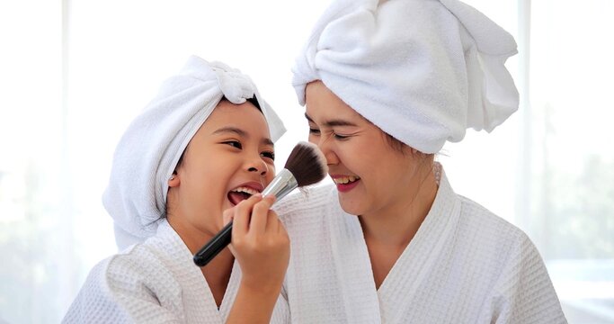 Happy Asian daughter and mother playing makeup after bathroom sitting on bed together at home, Family and beauty concept - Powered by Adobe