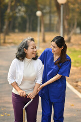 Careful caregiver taking care of elderly woman patient during walking outdoor. Assistance and rehabilitation concept