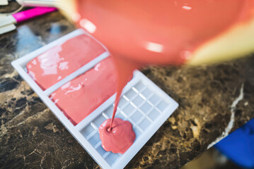 Home-made ruby chocolate bars. High angle view showing the process of pouring liquid pink chocolate to white moulds. High quality photo