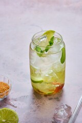 Non-alcoholic soft drink with lime slices, ice cubes and fresh mint in a jar-shaped glass on a brown background.