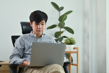 Portrait of handsome man freelancer in smart casual wears sitting in home office and using laptop