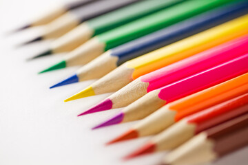 Colored pencils color of rainbow for drawing, laid out side by side one to other on white background, close-up selective focus