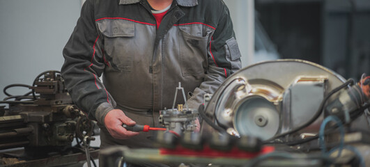 Hands of a mechanic are visible adjusting or setting idle or air mixture screws on a vintage...