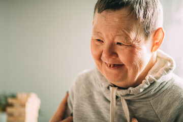an elderly woman with Down syndrome, accompanied by an assistant who supports her, holds her hands