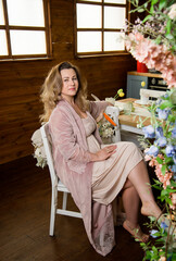 brunette woman in pink dressing gown sitting on a chair in kitchen with easter decoration and spring flowers