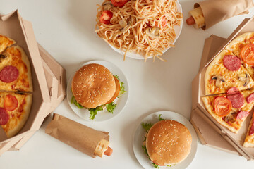 Top view image of pizza with mushrooms, cheese and meat, spaghetti with tomatoes, hamburger with fries, sausage in dough. Tasty and delicious dinner with junk food.