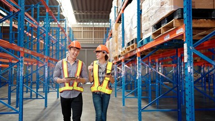 Two professional workers with list checking stock condition in business factory industry warehouse wearing engineer suit and helmet for safety