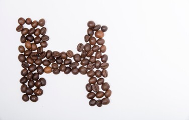 H is a capital letter of the English alphabet made up of natural roasted coffee beans that lie on a white background. Plenty of space to put text or pictures, top view and studio photography.