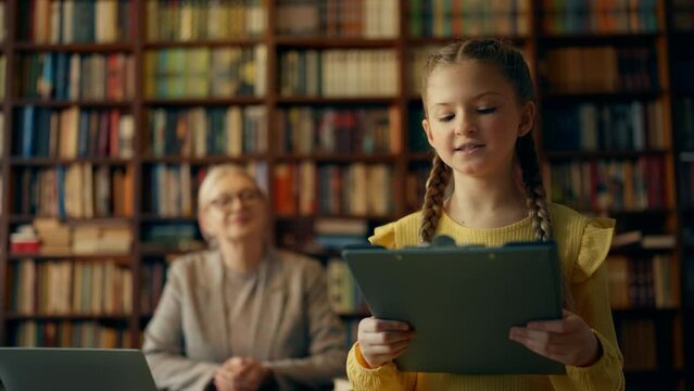 Schoolgirl presenting school project in class, teacher listening on background