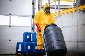 Worker in protective uniform, gas mask, gloves and boots working with barrels of toxic waste on...