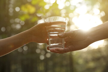Man giving woman glass of fresh water in forest on sunny day, closeup