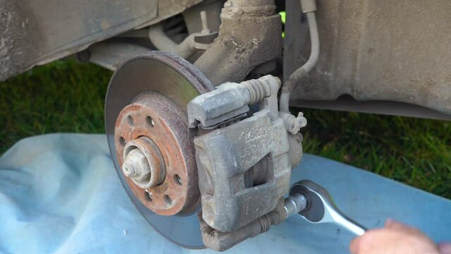 dismantling of the car caliper,a locksmith with a ratchet wrench unscrews a brake caliper on a car, replacing a brake caliper on a car