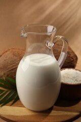 Obraz na płótnie Canvas Glass jug of delicious vegan milk near coconuts on brown background