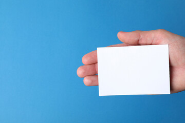 Man holding paper card on blue background, closeup. Mockup for design