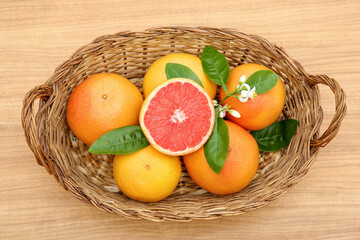 Wicker basket with fresh ripe grapefruits and green leaves on wooden table, top view