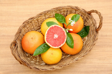 Wicker basket with fresh ripe grapefruits and green leaves on wooden table, top view