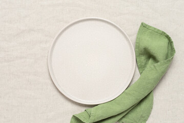 Empty beige plate with green napkin. Beige linen background. Top view, flat lay, copy space.
