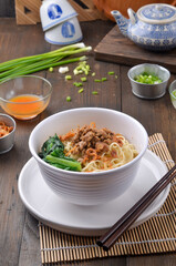 Chicken Noddle served with vegetables, meat chopped, and pangsit isolated on wooden background
