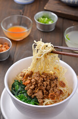 Chicken Noddle served with vegetables, meat chopped, and pangsit isolated on wooden background
