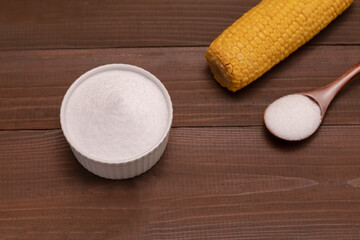 Organic sweetener zero calorie Erythritol, produced by fermentation from corn, called dextrose in ceramic bowl, wooden spoon,corncob on brown wooden table.Sugar substitute.Horizontal plane,top view.