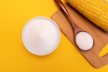 Fototapeta na wymiar Natural sweetener Erythritol, produced by fermentation from corn in ceramic bowl, wooden spoon, corncob on yellow orange background. Sugar substitute. Horizontal plane, top view.