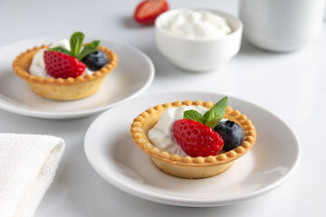 tartlets with buttercream, blueberries, strawberries, mint on a white background