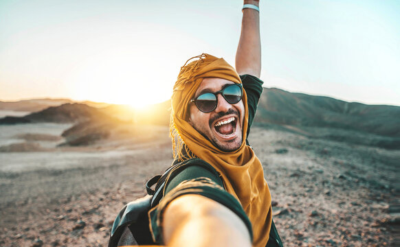 Handsome man taking selfie pic with smart mobile phone outside at golden hour time - Traveler guy with backpack enjoying day out on summer vacation - Happy tourist having fun at summertime holiday